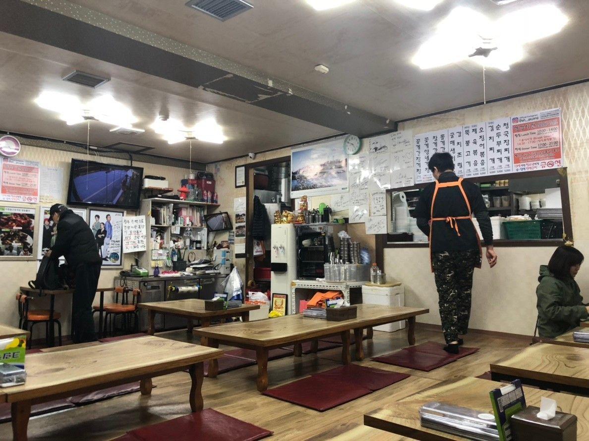 บรรยากาศภายในของร้าน Ahyundong Ganjang Gejang ที่มีเมนูเขียนอยู่บนผนังและลูกค้ากำลังนั่งรับประทานอาหารบนโต๊ะไม้